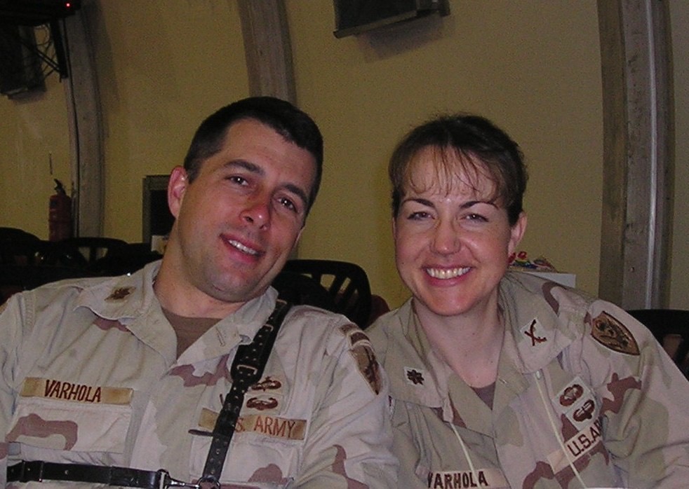Two U.S. Army soldiers smiling together in military uniforms, sitting in a casual setting, showcasing camaraderie and friendship.